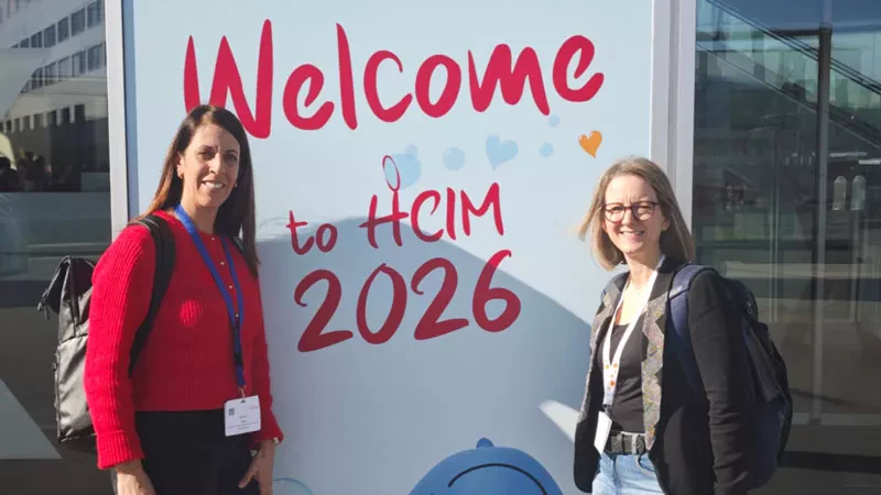 Sandra Zoni et Julie Desarzens devant l'affiche du congrès HCIM 2026